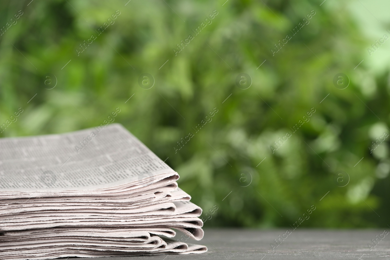 Photo of Stack of newspapers on grey table against blurred green background, space for text. Journalist's work