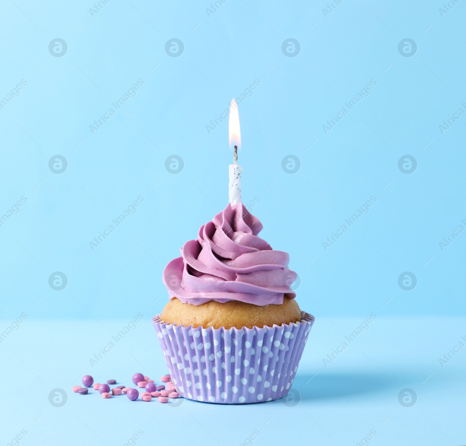 Photo of Delicious birthday cupcake with burning candle and sprinkles on light blue background