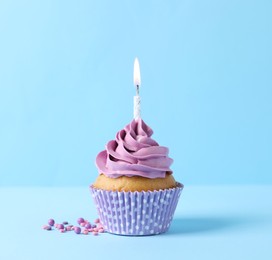 Delicious birthday cupcake with burning candle and sprinkles on light blue background