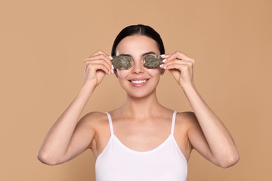 Photo of Beautiful young woman putting green tea bags on skin around eyes against beige background