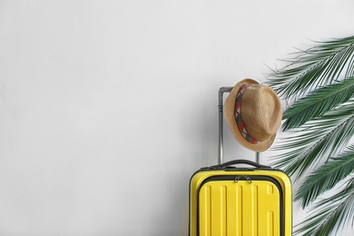 Photo of Bright yellow suitcase with hat and palm branches on light background