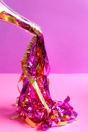 Photo of Champagne bottle with bright party streamers on pink background