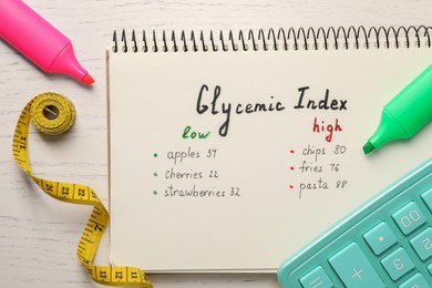 Photo of List with products of low and high glycemic index in notebook, markers, measuring tape and calculator on white wooden table, flat lay