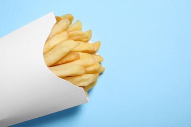 Photo of Paper cup with French fries on light blue table, closeup. Space for text