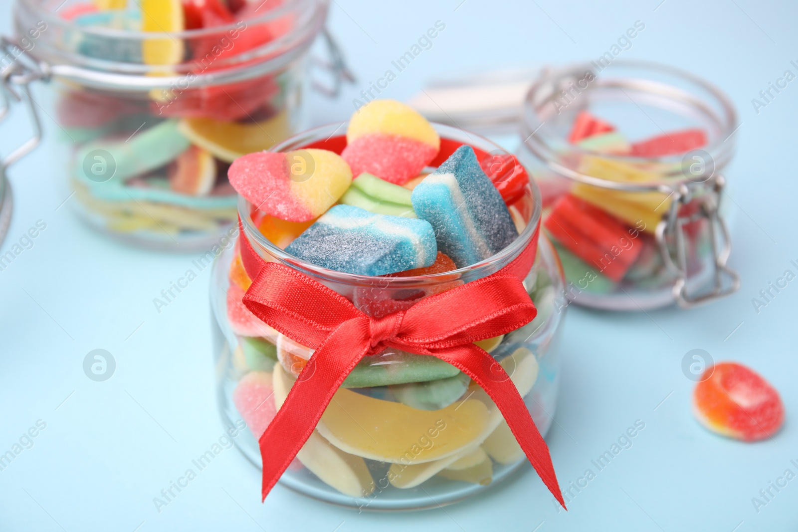 Photo of Tasty colorful jelly candies in glass jars on light blue table