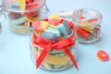 Photo of Tasty colorful jelly candies in glass jars on light blue table