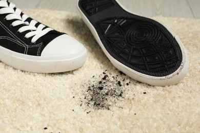 Photo of Black sneakers and mud on beige carpet, closeup