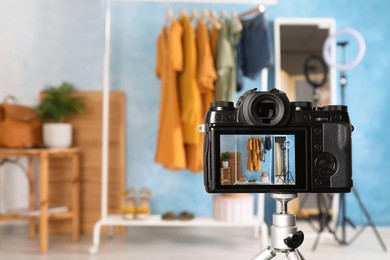 Rack with stylish clothes and mirror near light blue wall indoors, focus on camera screen. Space for text