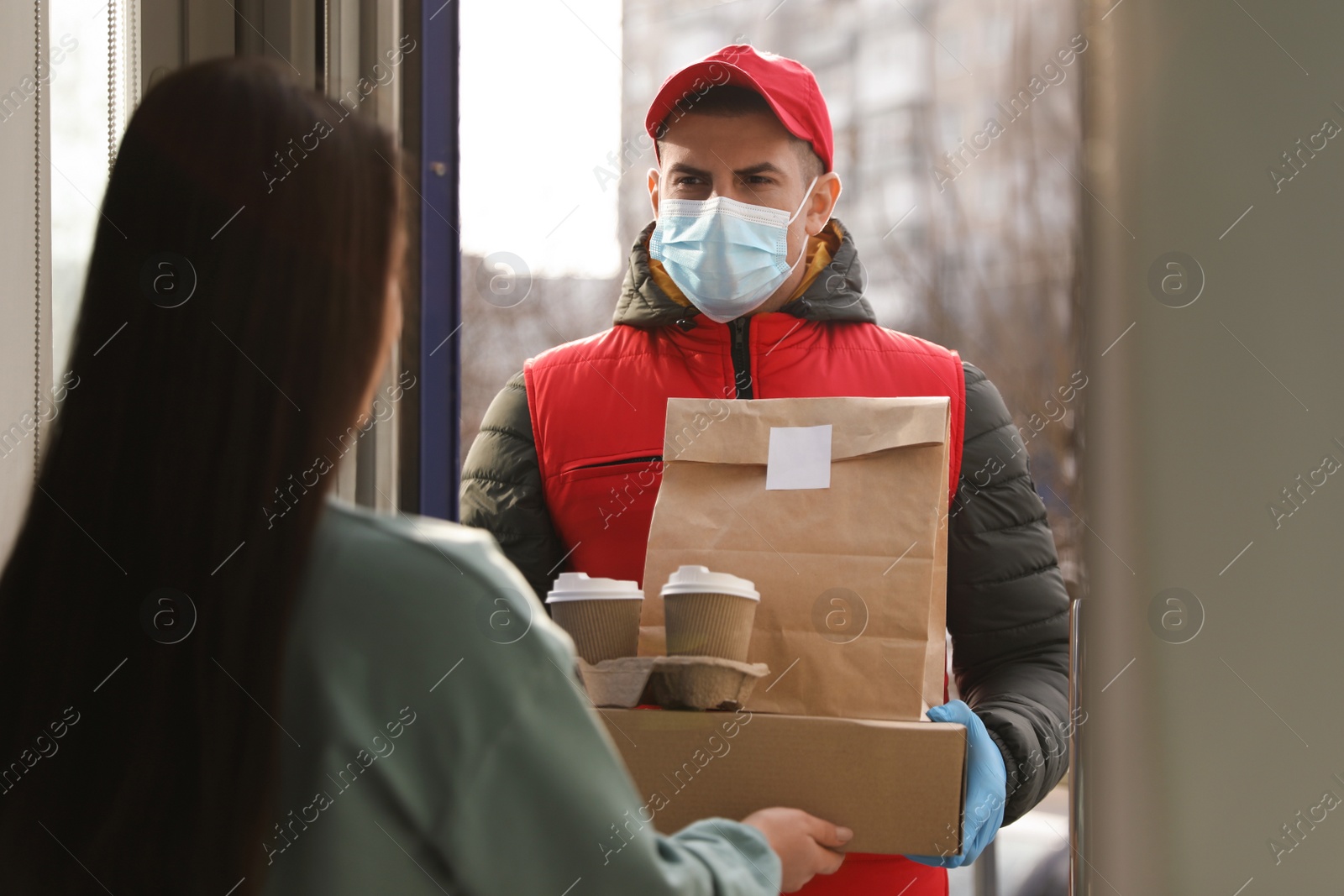 Photo of Courier in medical mask giving to woman her order at doorway. Delivery service during Covid-19 quarantine