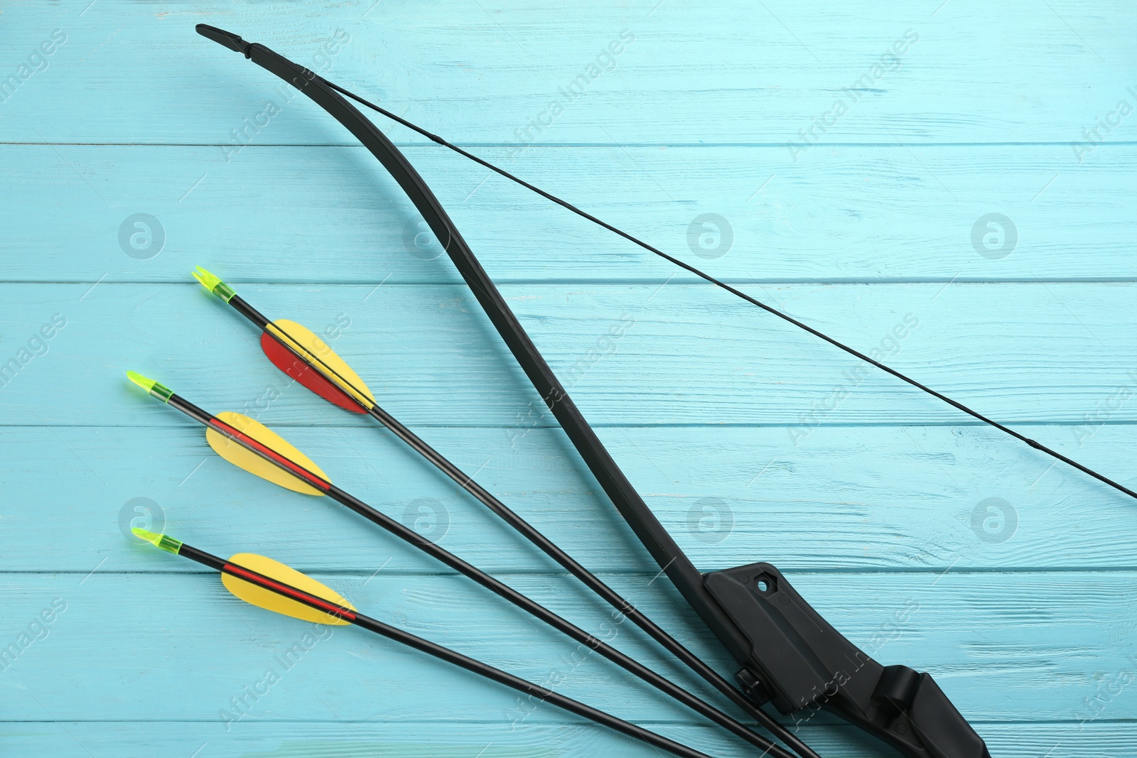 Photo of Plastic arrows and bow on turquoise wooden table, flat lay. Archery sports equipment
