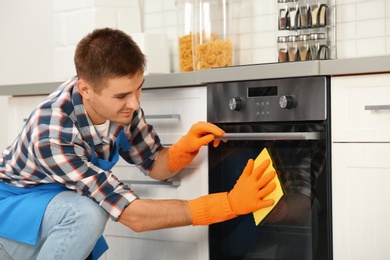 Man cleaning kitchen oven with rag in house