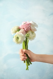 Young woman holding ranunculus flowers on color background