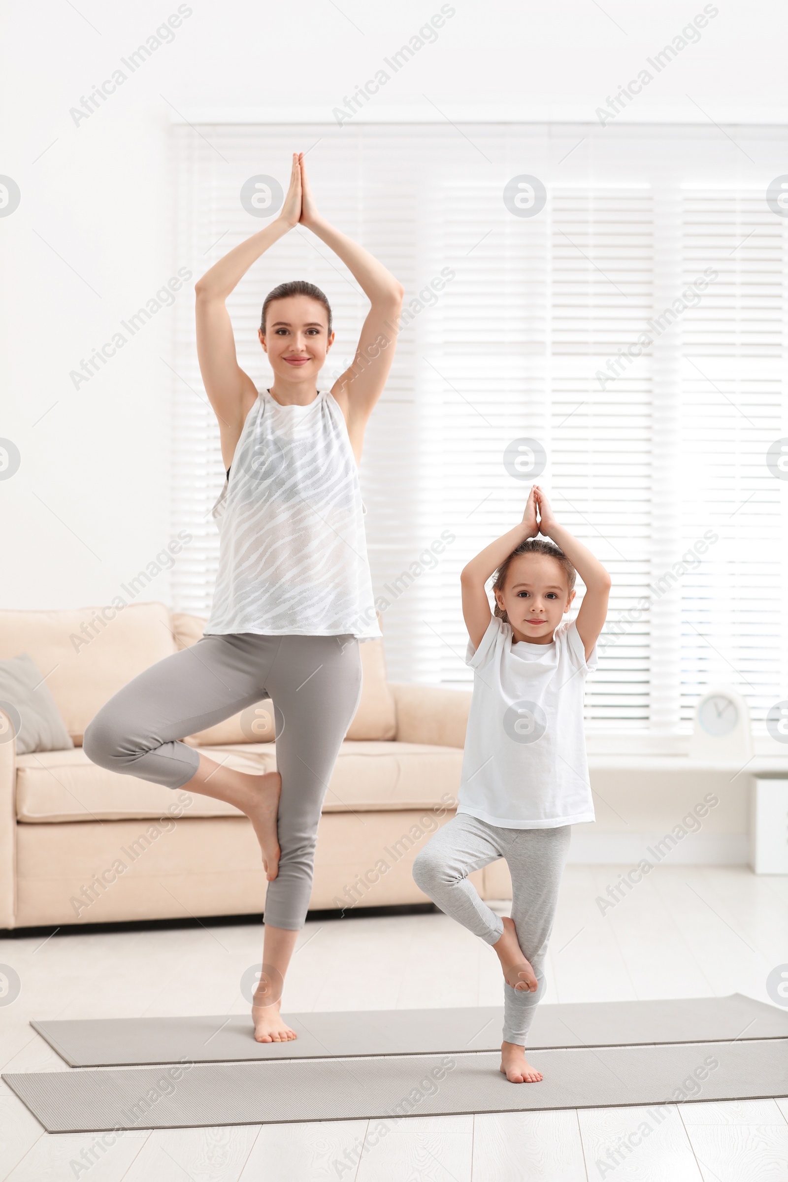 Photo of Young mother with little daughter practicing yoga at home