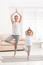 Young mother with little daughter practicing yoga at home