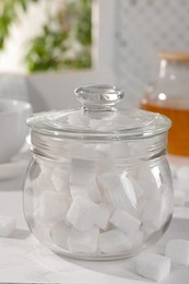 Glass jar of refined sugar cubes on white table