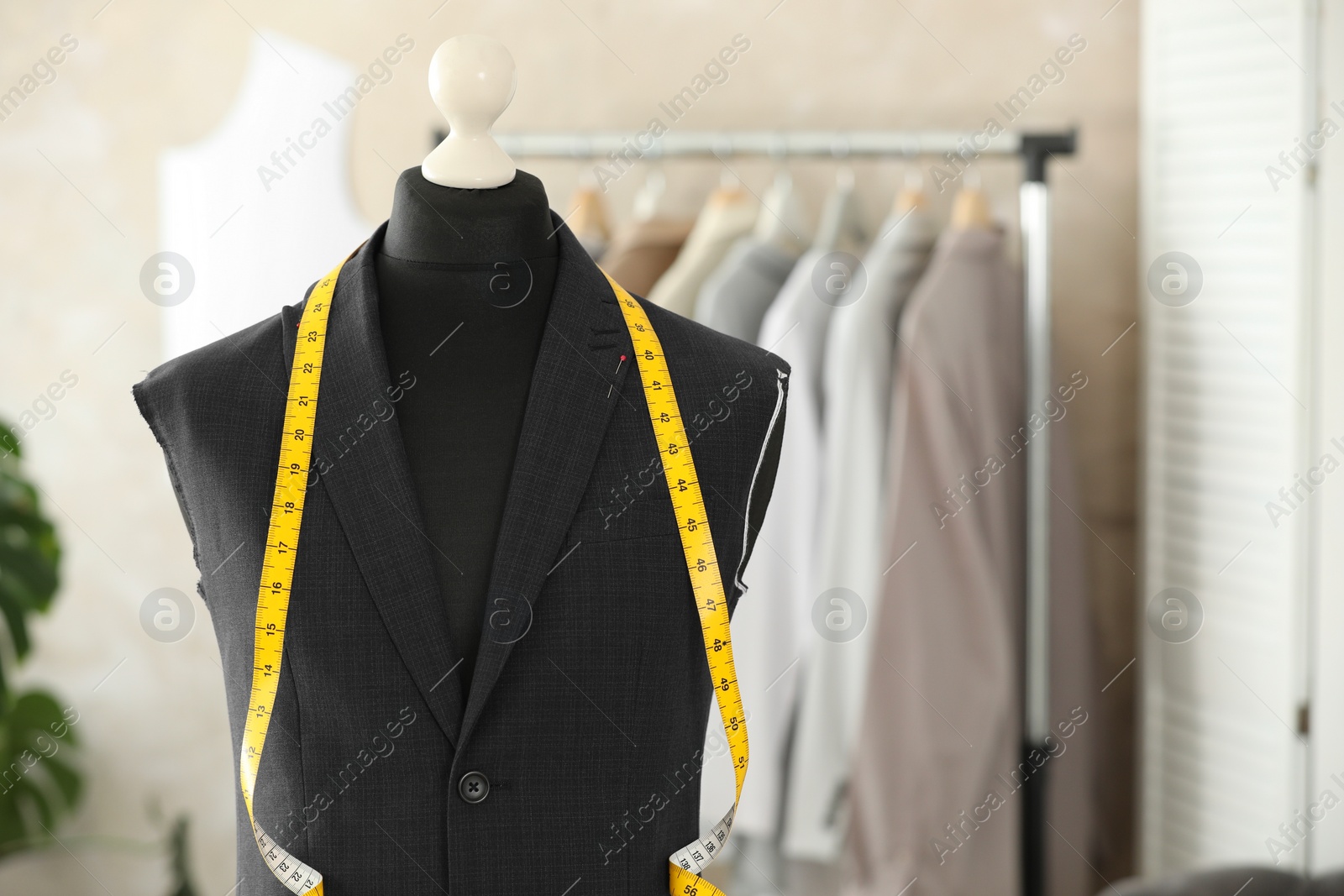 Photo of Mannequin with unfinished suit jacket and measuring tape in tailor shop, space for text