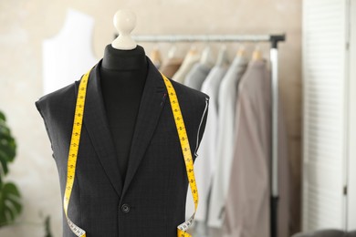 Photo of Mannequin with unfinished suit jacket and measuring tape in tailor shop, space for text