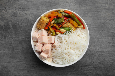 Photo of Tasty cooked rice noodles with chicken and vegetables on grey table, top view