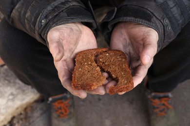 Photo of Poor homeless man holding piece of bread outdoors, top view