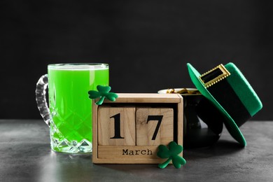 Photo of St. Patrick's day celebrating on March 17. Green beer, wooden block calendar, leprechaun hat, pot of gold and decorative clover leaves on grey table