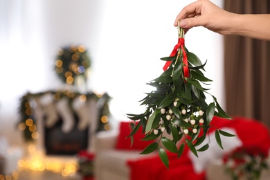 Photo of Woman holding mistletoe bunch in room with Christmas decorations, closeup. Space for text