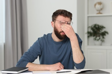 Overwhelmed man with glasses at table indoors