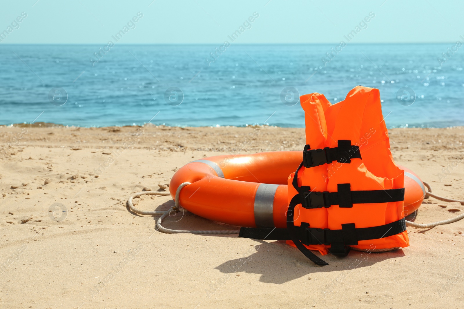 Photo of Orange life jacket and buoy on sandy beach near sea. Emergency rescue equipment