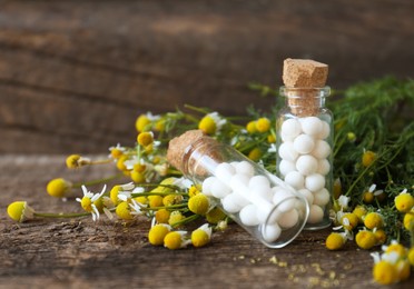 Photo of Bottles with homeopathic remedy and chamomile flowers on wooden table, closeup. Space for text