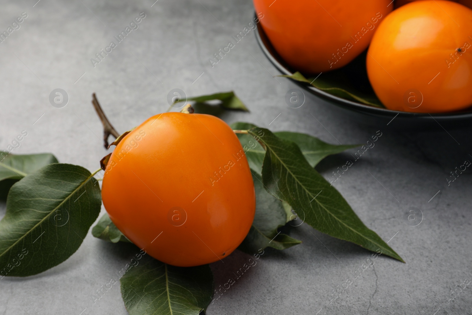 Photo of Delicious ripe persimmons in bowl on light gray table
