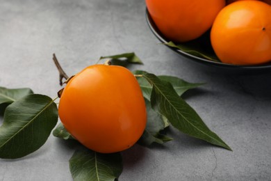 Delicious ripe persimmons in bowl on light gray table