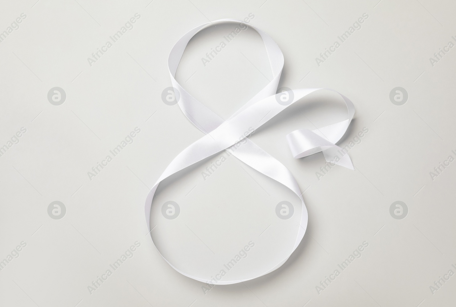 Photo of Number 8 made of white ribbon on light grey background, top view. International Women's day