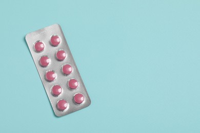 Photo of Pink pills in blister on turquoise background, top view. Space for text