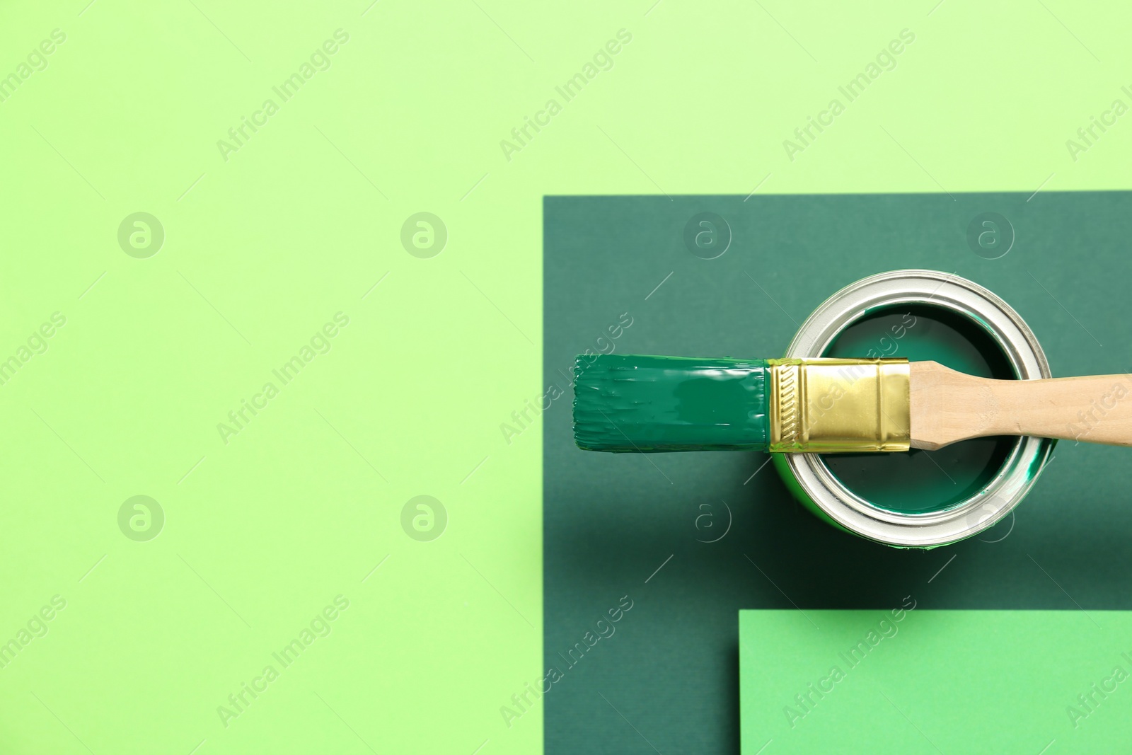 Photo of Can of green paint with brush on color background, top view. Space for text