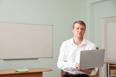 Portrait of male teacher with laptop in modern classroom