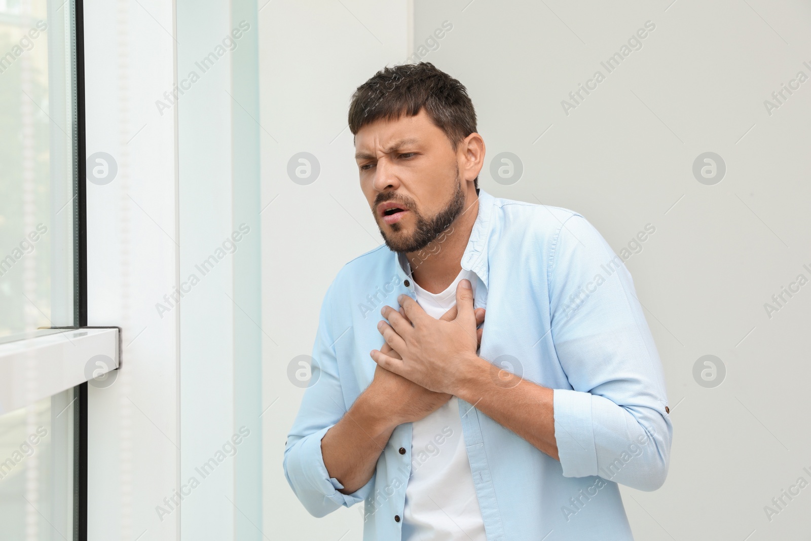 Photo of Man suffering from pain during breathing near window