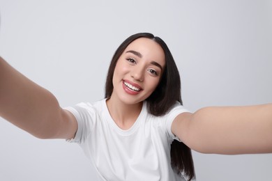 Smiling young woman taking selfie on white background