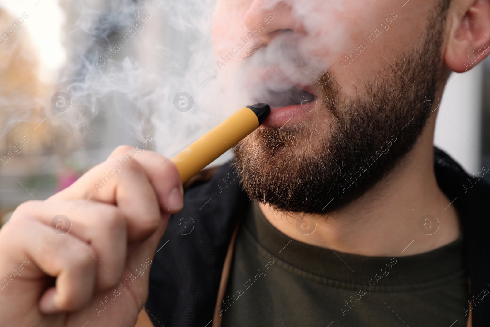 Photo of Handsome young man using disposable electronic cigarette outdoors, closeup