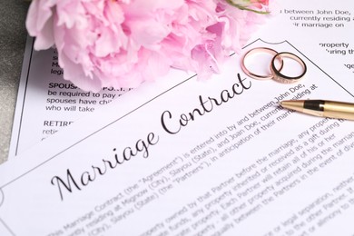 Photo of Marriage contract, wedding rings, pen and flowers on table, closeup