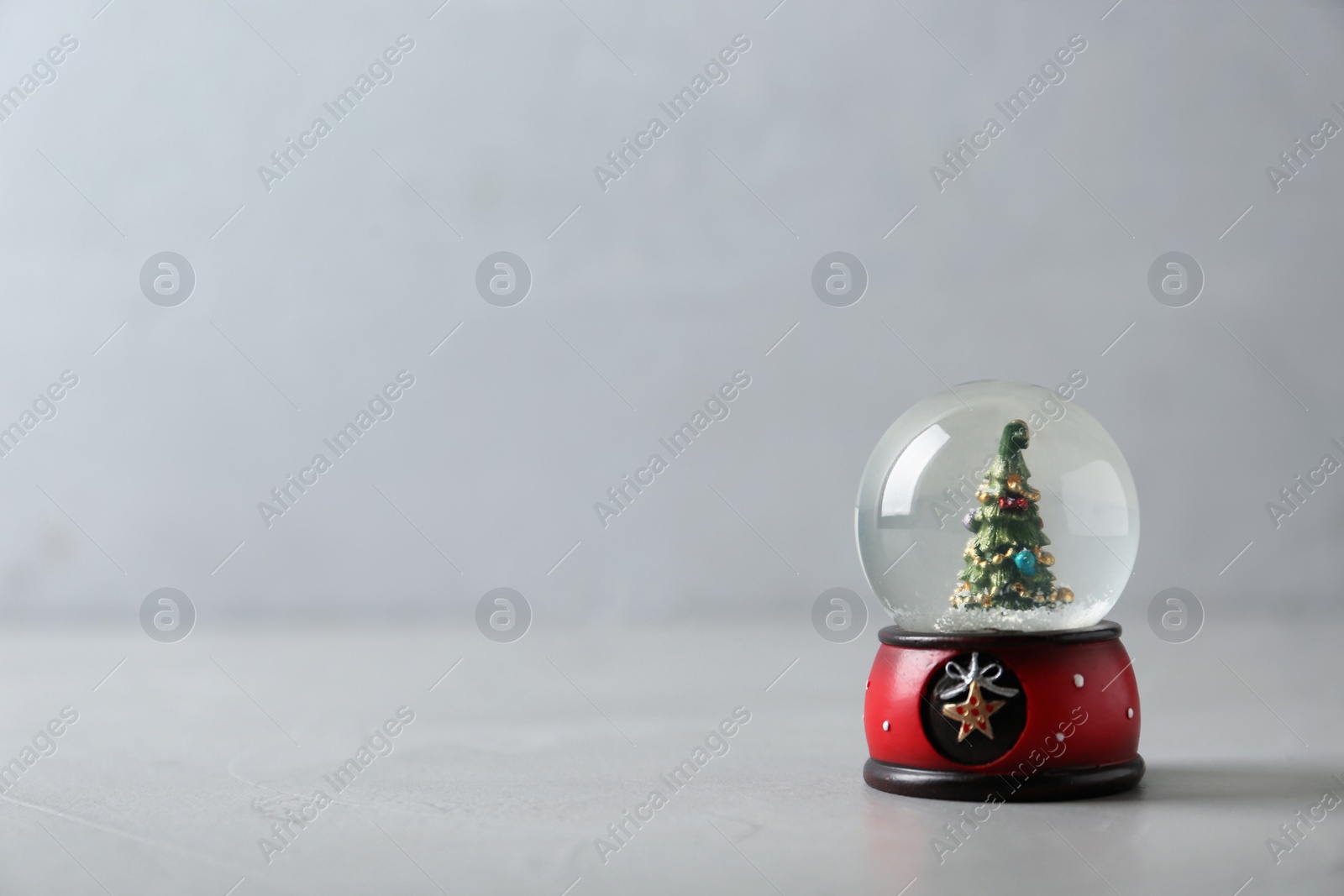 Photo of Snow globe with Christmas tree on grey table, space for text