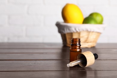 Bottle of essential oil with different citrus fruits on wooden table. Space for text