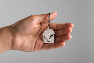 Photo of Woman holding metallic keychain in shape of house on grey background, closeup