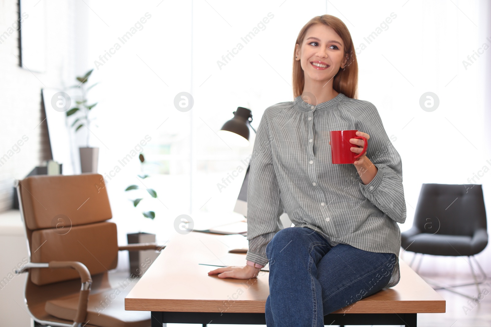Photo of Young woman with cup of drink relaxing in office during break