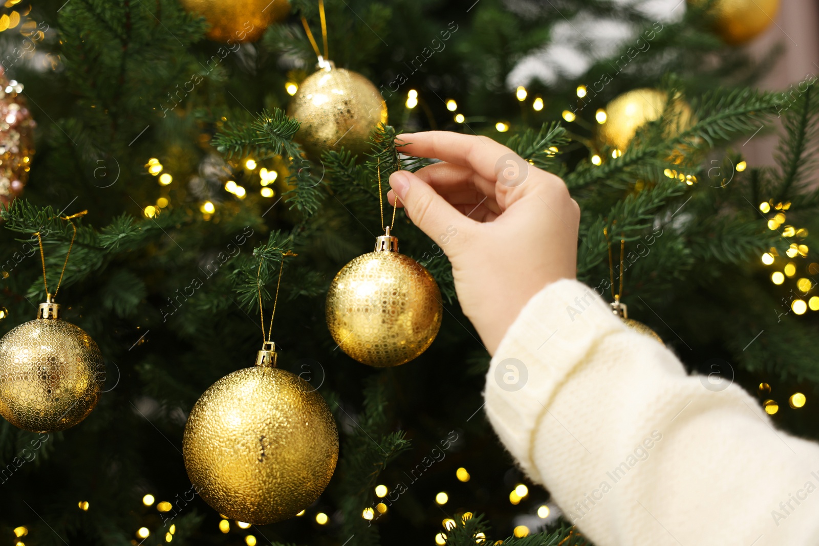 Photo of Woman decorating fir tree with golden Christmas ball, closeup