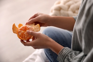 Woman peeling fresh tangerine on blurred background, closeup