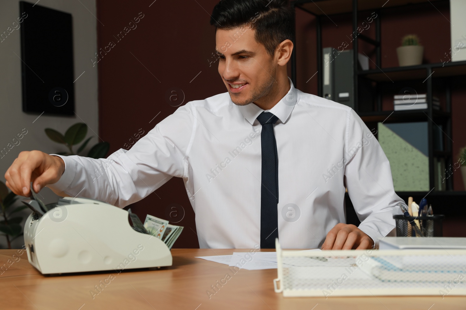 Photo of Man putting money into banknote counter at wooden table indoors