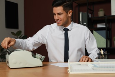 Man putting money into banknote counter at wooden table indoors