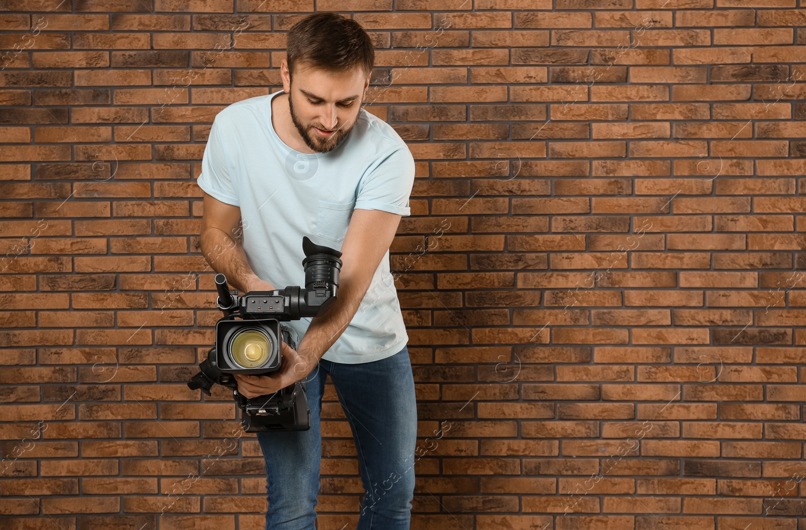 Photo of Operator with professional video camera near brick wall, space for text