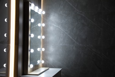 Photo of Modern mirror with light bulbs on grey chest of drawers in room. Space for text