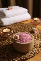 Photo of Bowl of pink sea salt, roses, burning candles and towels on wooden table
