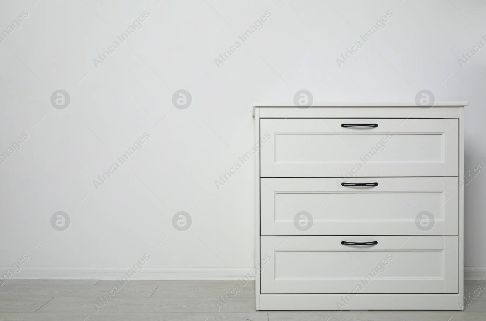 Photo of Modern wooden chest of drawers at light wall. Space for text